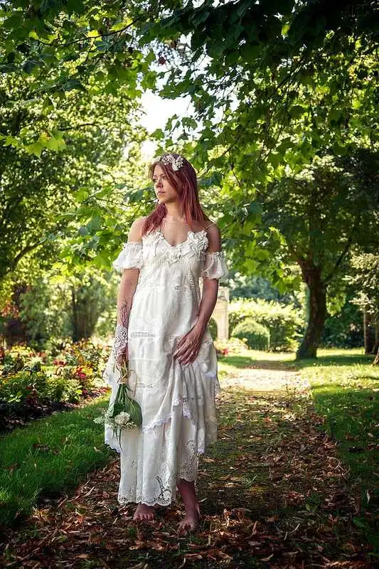 Robe de mari&eacute;e boh&egrave;me chic avec dentelle florale et manches tombantes, port&eacute;e dans un jardin verdoyant